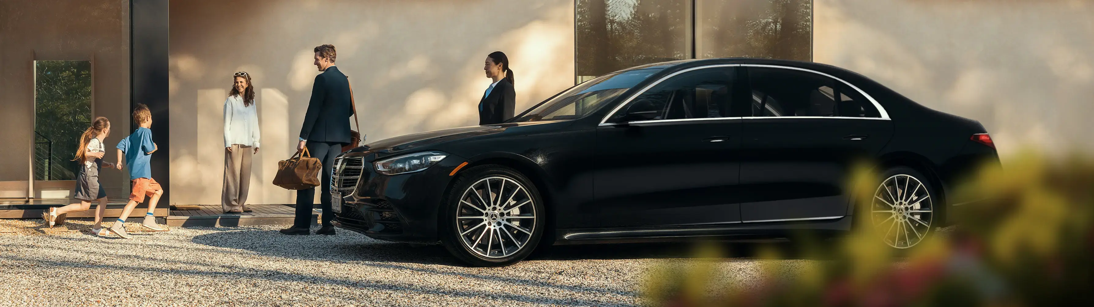 Blacklane chauffeur and family standing around a sleek, black Mercedes limo.